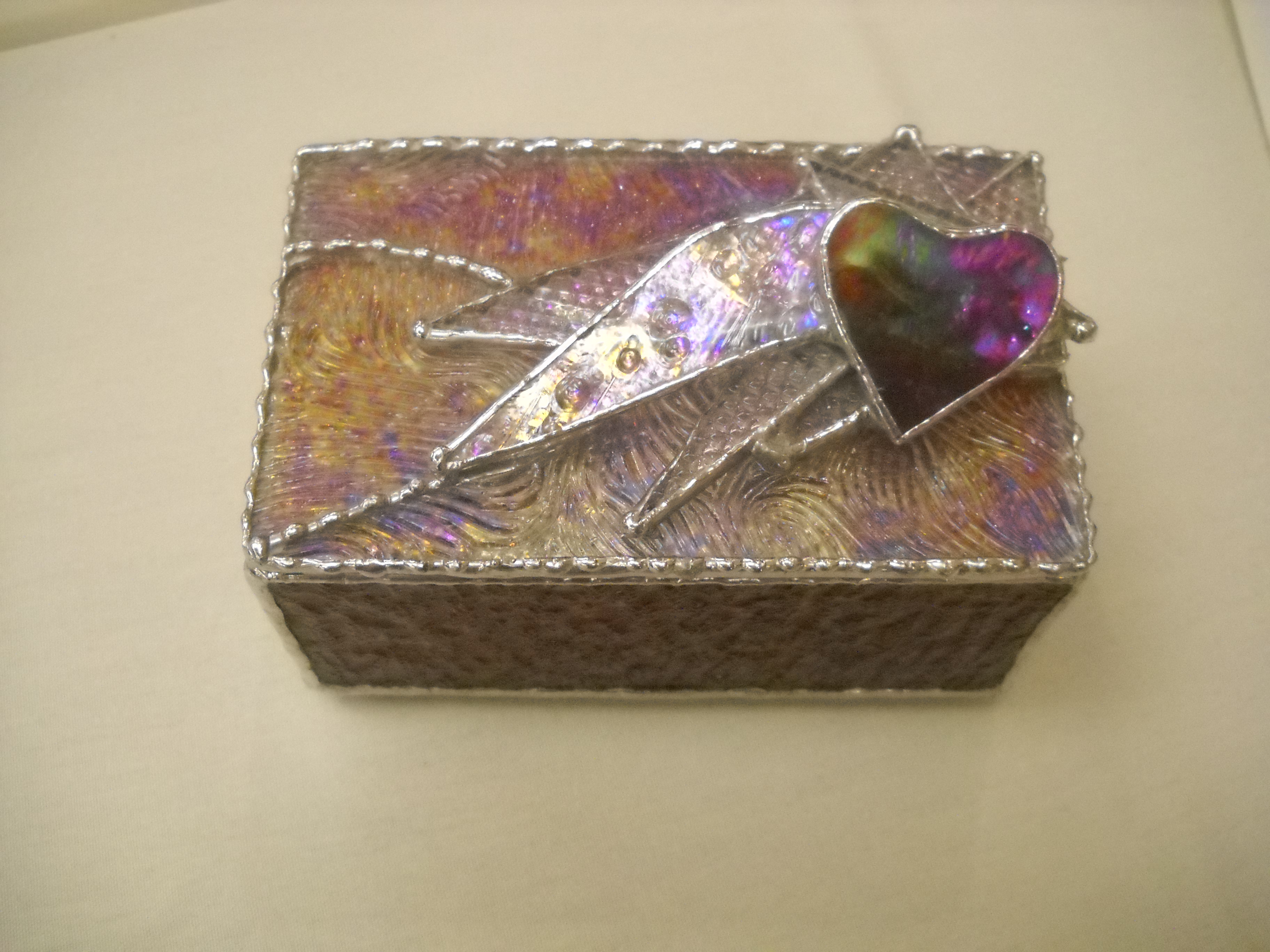 A glass jewelry box with a heart on top. The box is a purple and pink color